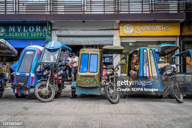 Motorcycle "trike" drivers take a break while waiting for customers outside of a busy public bus station. Daily life in Moalboal District, Cebu,...