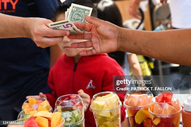 Customer pays cash for a container of fresh fruit from a street vendor along Hollywood Blvd on July 13, 2022 in Los Angeles, California. US consumer...