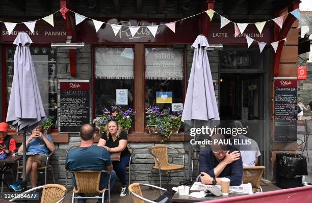 People sit outside the Relish Cafe in the town centre of Keswick in the Lake District, north west England on June 20, 2022 as an advert for staff...