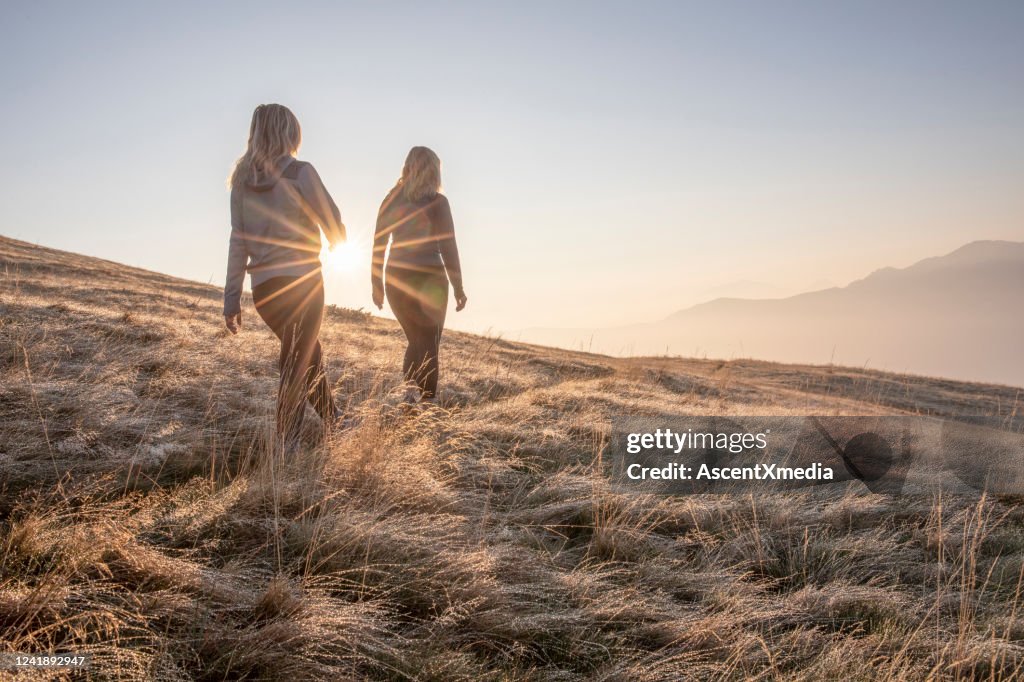 Wanderinnen wandern bei Sonnenaufgang auf der Graswiese