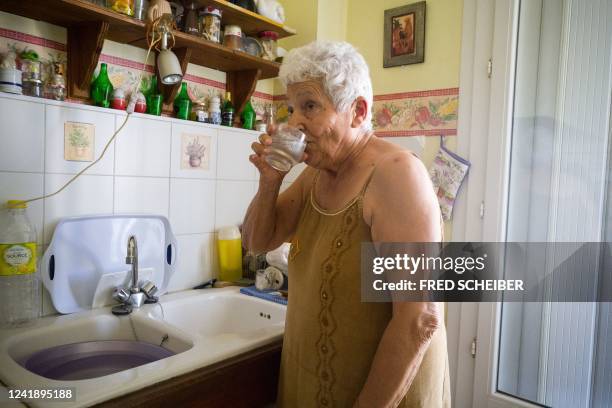 Jackye Lafon, an 81-year-old retiree, drinks water in her flat of the Cite Bourbaki in the Minimes district of Toulouse on July 14, 2022. - France is...