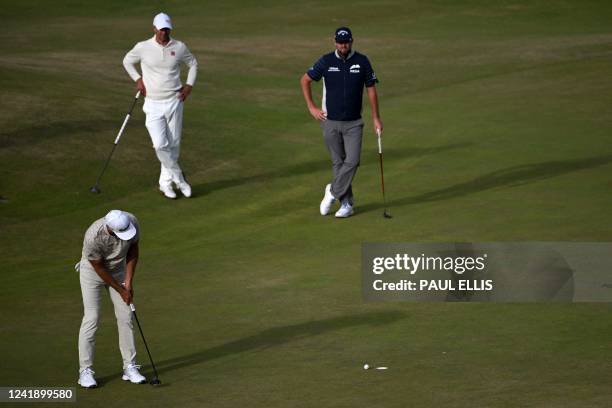 Australia's Adam Scott and Australia's Marc Leishman look on as US golfer Dustin Johnson putts on the 17th green during his opening round on the...