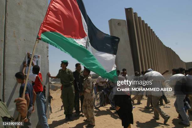 Palestinians, one of them holding a national flag, gather next to the concrete wall, built by Israel, that divides Palestinian Rafah from the...