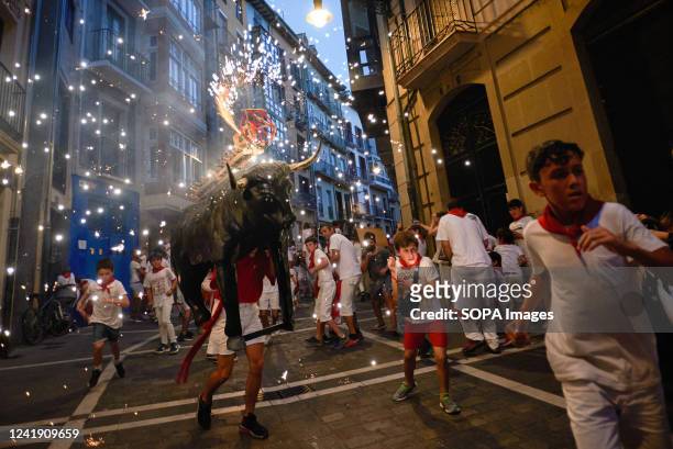 Children run in front of the fire bull during the San Fermín festivities. A man carrying a bull-shaped structure loaded with fireworks called Toro de...
