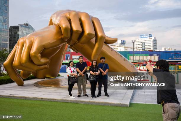 Group of people pose in front of a bronze sculpture by artist Hwang Man-seok, modeled after the signature horse-riding hand motion of the "Gangnam...