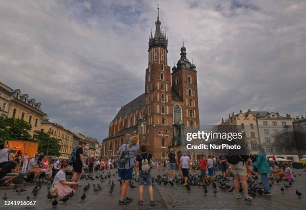Visitors feed pigeons and listen to St. Mary's trumpet call in Krakow's UNESCO listed Market Square. On Thursday, July 14 in Krakow, Poland.