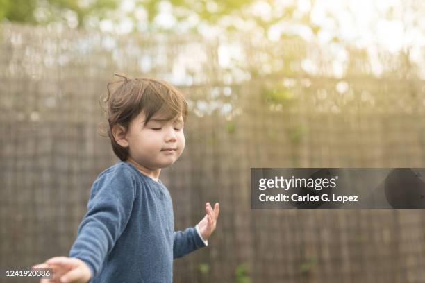 child wearing blue jumper closes her eyes and smells the fresh air as she runs around garden - fresh air breathing stockfoto's en -beelden