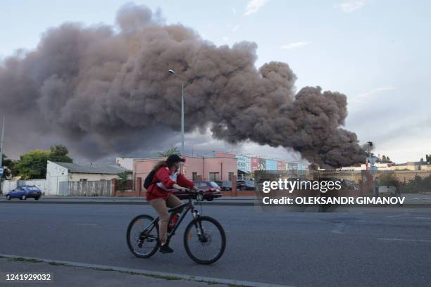 Woman riding a bicycle drives past a cloud of smoke from a fire in the background after a missile strike on a warehouse of an industrial and trading...