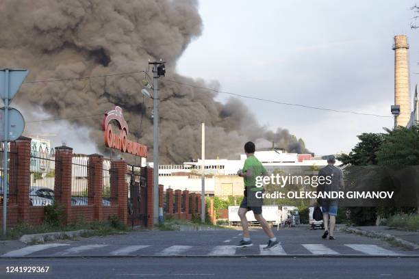 Man jogs past a cloud of smoke from a fire in the background after a missile strike on a warehouse of an industrial and trading company in Odessa on...