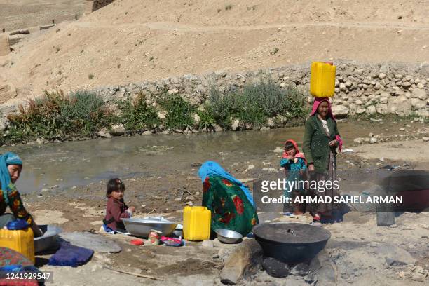 Afghan women wash clothes as children sit by a stream in the Paytaw village of Yakawlang district of Bamiyan province on July 15, 2022. / "The...