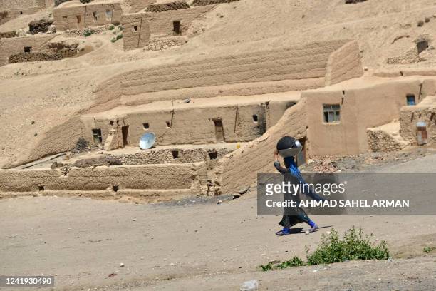 An Afghan Hazara woman carries washed utensils as she walks home in the Paytaw village of Yakawlang District of Bamiyan Province on July 15, 2022. /...