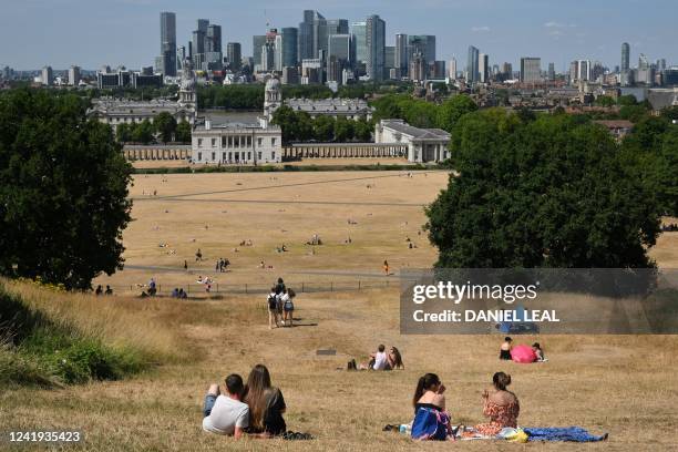 People look out toward the Old Royal Naval College, and the Canary Wharf financial district, past the sun-scorched grass in Greenwich Park, south...