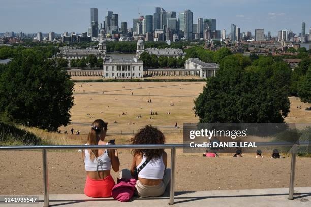 People look out toward the Old Royal Naval College, and the Canary Wharf financial district, past the sun-scorched grass in Greenwich Park, south...