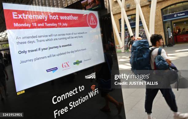 Rail passengers pass an electronic sign warning of 'Extremely hot weather' forecast for July 18 and 19, and advising commuters to only travel for...