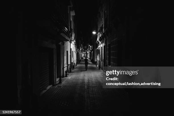 woman walking alone in the street late at night.narrow dark alley,unsafe female silhouette.empty streets.woman pedestrian alone.police hour.assault situation,violence against women concept. - wall night stock-fotos und bilder