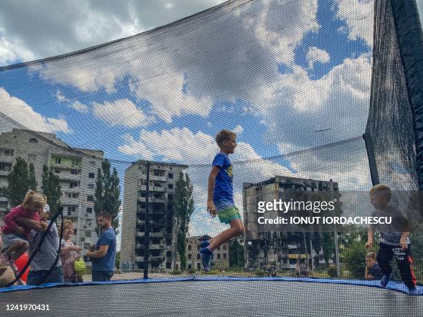 Child jumps on a trampoline against the backdrop of destroyed buildings in Borodianka, northwest of Kyiv on July 16, 2022. - Music teacher Oksana...