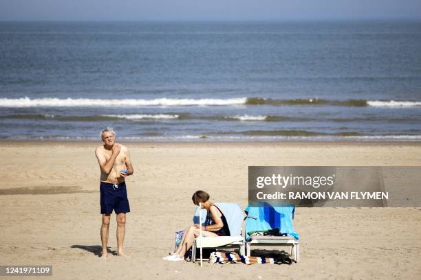 Man rubs in sunblock as a woman arranges her sunbed on the beach, as Europe braces for a heatwave, in Zandvoort on July 18, 2022. - The heatwave,...