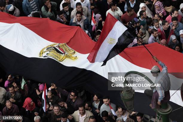 An Egyptian protester waves a national flag as he sits on an electricity pole during demonstrations by thousands of anti-government supporters who...