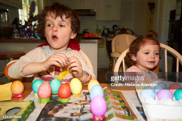 young cousins dying eggs for easter at kitchen table camera flash both looking away from the camera sitting at kitchen table face to face - melanie cousins 個照片及圖片檔
