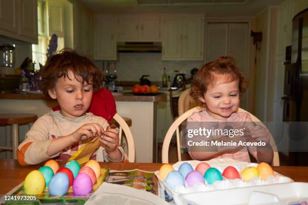 young cousins dying eggs for easter at kitchen table camera flash both kids the little girl and boy laughing smiling talking while dying eggs - melanie cousins 個照片及圖片檔