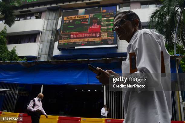 Man with his phone walks past Bombay Stock Exchange office in Mumbai, India, 18 July, 2022. The S&amp;P BSE Sensex jumped 760 points to end at 54,521...