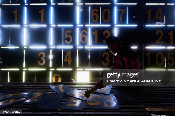 Admire Mupembe, a scoreboard operator, sorts out numbers from within the manual scoreboard during the cricket T20 World Cup Qualifier tournament at...