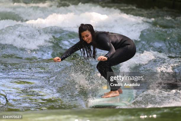 Surfer rides a wave of her surf board at Eisbach which is an artificial river and also flows for a long stretch through the English Garden in Munich,...