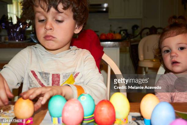 young cousins dying eggs for easter at kitchen table camera flash close up boy is looking down at the dyed eggs little girl is looking behind the camera - melanie cousins 個照片及圖片檔