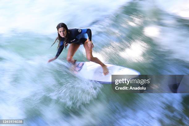 Surfer rides her surfboard on the wave at Eisbach which is an artificial river and also flows for a long stretch through the English Garden in...