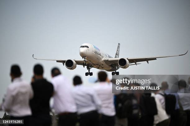 Visitors look at a Airbus A350 plane flying over during the airshow of the Farnborough Airshow, in Farnborough, on July 18, 2022.