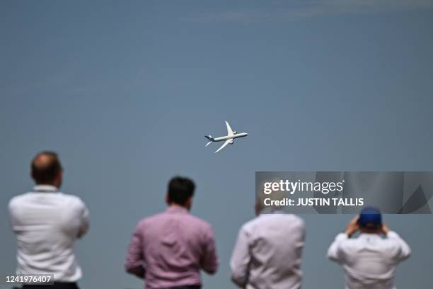 Visitors look at a Boeing 777X plane flying over during the airshow of the Farnborough Airshow, in Farnborough, on July 18, 2022.
