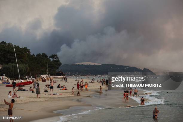 This photograph taken on July 18, 2022 shows people swim on the Moulleau's beach as the smoke rising from the forest fire in La Teste-de-Buch, seen...