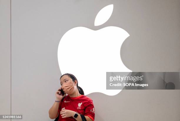 Woman uses a smartphone as she stands in front of the American multinational technology company Apple logo and store in Hong Kong.