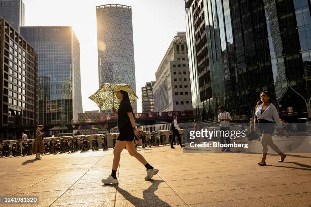 Pedestrian uses a umbrella to protect herself from the sun, at Canary Wharf, during a heatwave in London, UK, on Monday, July 18, 2022. Extreme heat...