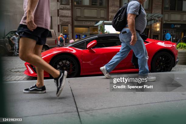 People walk by a Lamborghini car along Wall Street in the Financial District of Manhattan on July 18, 2022 in New York City. Global markets continue...