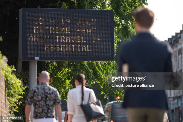 July 2022, Great Britain, London: Passersby walk towards an LED sign saying "18 -19 July extreme heat only travel if essential". In the London...