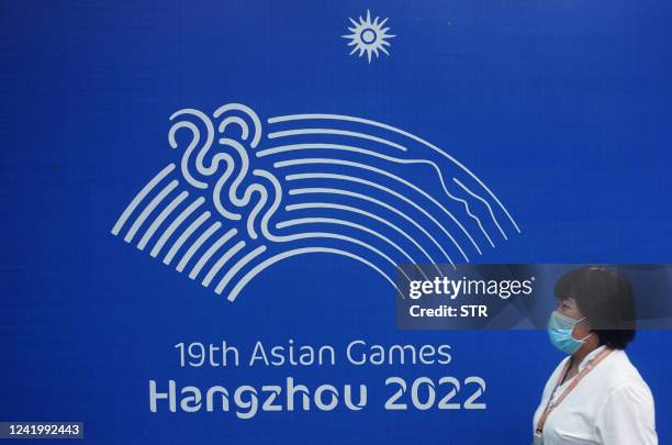 This photo taken on July 18, 2022 shows a woman walking past a logo of the 2022 Asian Games in Hangzhou, in China's eastern Zhejiang province. -...