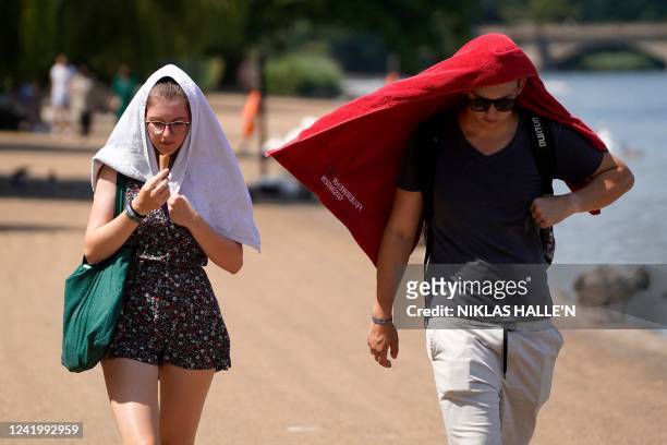 People cover their heads to shelter from the sun as they walk past the Serpentine lake in Hyde Park, west London, on July 19, 2022 as the country...