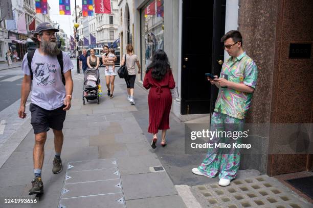 Man standing on Bond Street using two smartphones and wearing a colourful patterned silk outfit on 12th July 2022 in London, United Kingdom. Bond...