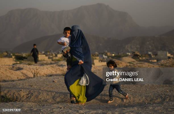 Burqa-clad Afghan woman along with children walks past a cemetery in Kabul on July 19, 2022.