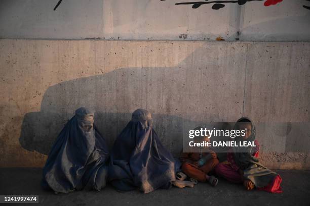 Burqa-clad Afghan women along with children sit along a street in Kabul on July 19, 2022.