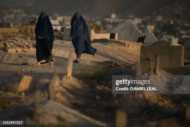Burqa-clad women walk along a cemetery during sunset in Kabul on July 19, 2022.