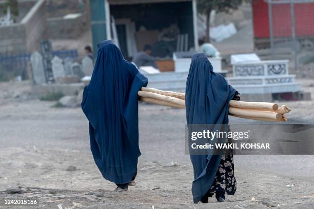 Afghan burqa-clad women carry wood along a street near Bala Hissar, an ancient fortress in Kabul on July 20, 2022.
