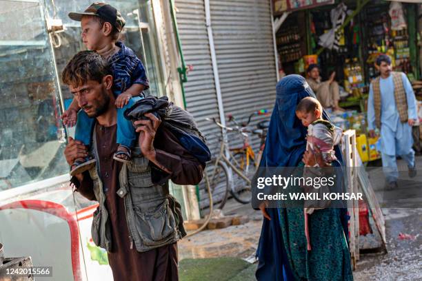 An Afghan man and burqa-clad woman carry their children as they walk past a market near the Pul-e Khishti mosque in Kabul on July 20, 2022.