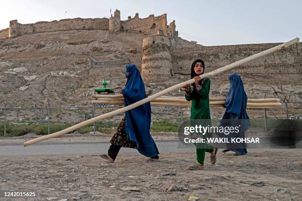 Afghan burqa-clad women carry wood along a street near Bala Hissar, an ancient fortress in Kabul on July 20, 2022.