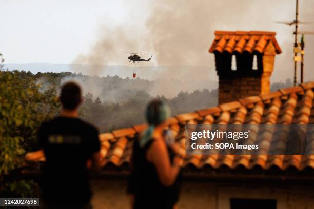People watch an army helicopter carrying a Bambi bucket flies over a large wildfire to extinguish the fire near Kostanjevica na Krasu. Over a...