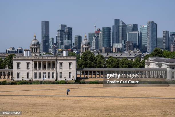 Woman shelters under an umbrella as she walks past dried grass in Greenwich Park on July 19, 2022 in London, England. Temperatures were expected to...