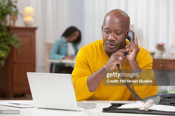 african american man using laptop and talking on telephone - landline phone home stock pictures, royalty-free photos & images