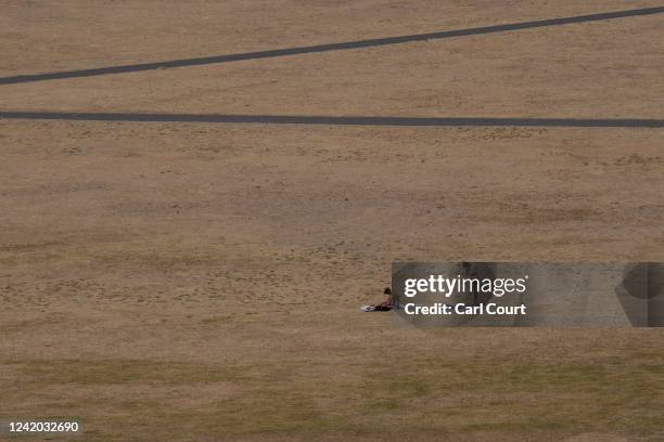 Woman applies suncream as she sunbathes on dried grass in Greenwich Park on July 19, 2022 in London, England. Temperatures were expected to hit 40C...
