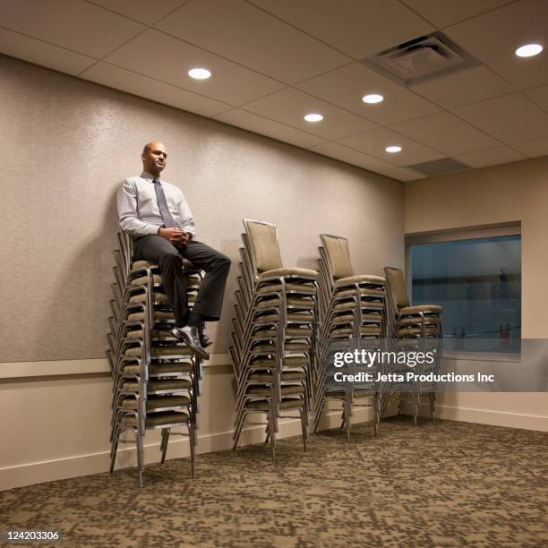mixed race businessman sitting on stack of chairs - leitende person stock-fotos und bilder